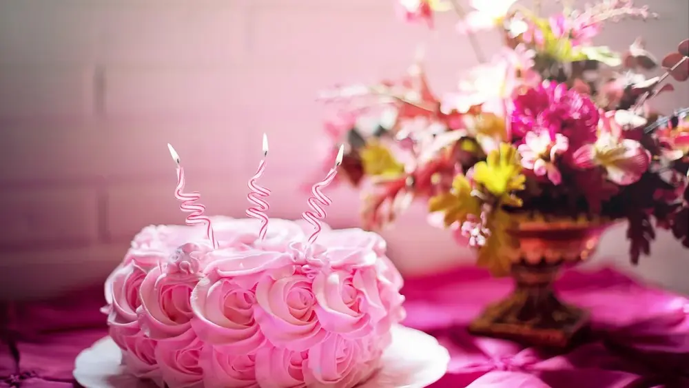 Bolo de aniversário rosa com velas e arranjo de flores ao lado