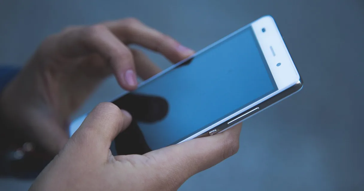 Mãos segurando um smartphone branco na posição horizontal, ilustrando o vídeo horizontal no iPhone